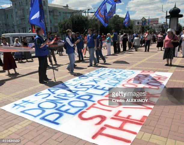 People stand in front of a sign reading "Save Donbass people - Stop the war" during a rally in the eastern Ukrainian city of Lugansk on June 29...