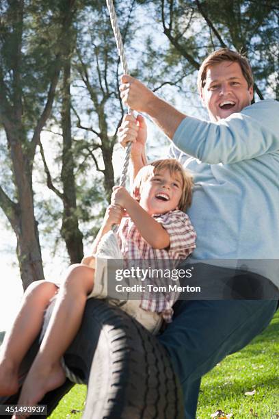 man and young boy outdoors at park playing on tire swing - tire swing stock pictures, royalty-free photos & images