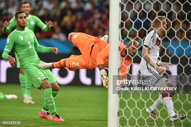 Germany's forward Andre Schuerrle celebrates after scoring a goal as Algeria's goalkeeper Rais Mbohli jumps to save the ball and Algeria's defender...