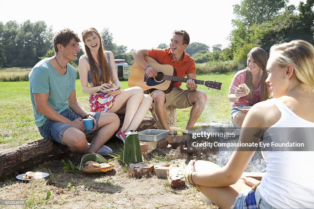 Group of friends with guitar relaxing by campfire