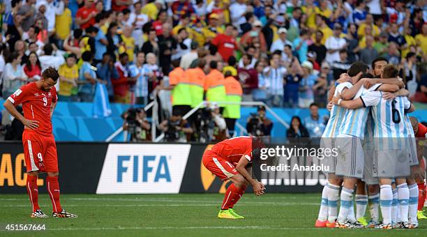 Haris Seferovic and Valon Behrami of Switzerland react as Argentina's players celebrate after a goal scored by Di Maria during the 2014 FIFA World...