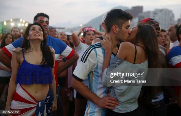 Fans watch next to a couple kissinf during the first half of their match against Belgium at FIFA Fan Fest on Copacabana Beach during the 2014 FIFA...