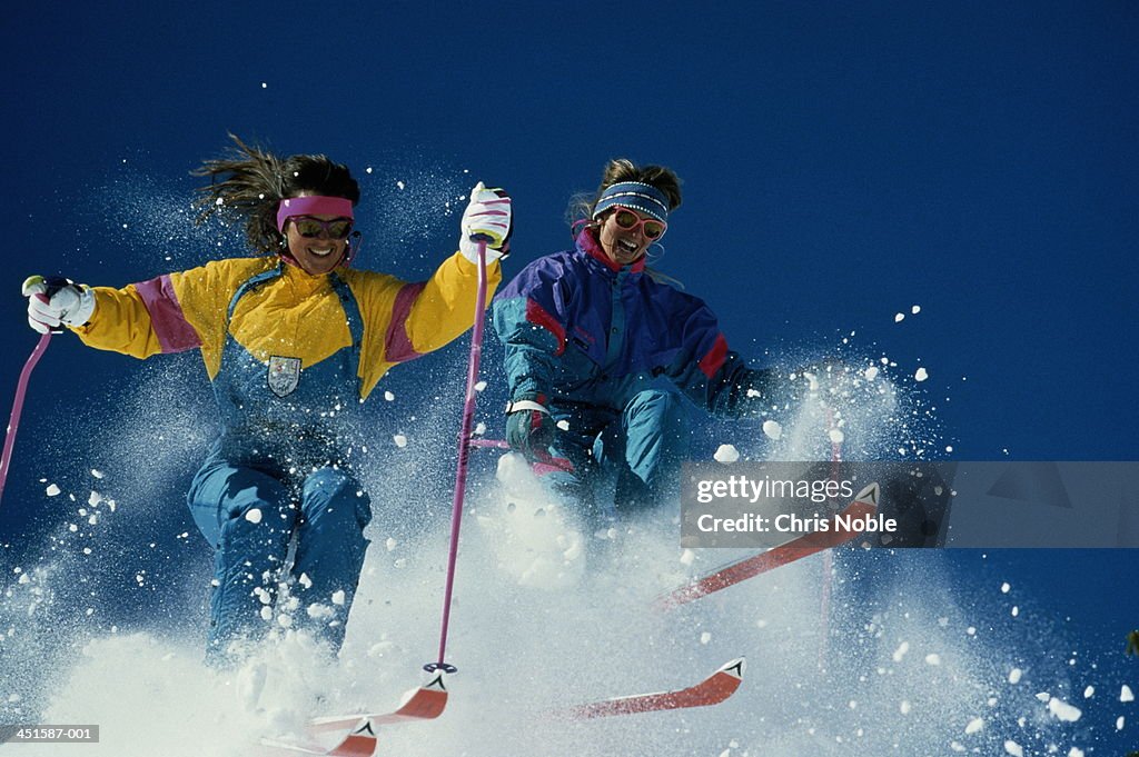 Two women skiing downhill, creating snow spray, low angle view