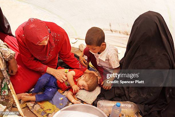 Family with sick children takes shelter under a sheet as thousands of Iraqis who have fled recent fighting in the cities of Mosul and Tal Afar try to...