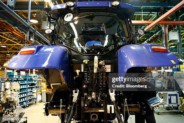 An employee works under the rear wheel arch of a New Holland tractor as it sits on the production line at CNH Industrial NV's assembly plant in...