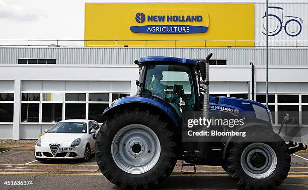 Newly manufactured New Holland tractor drives past a parked Alfa Romeo Giulietta automobile, outside the entrance to CNH Industrial NV's assembly...