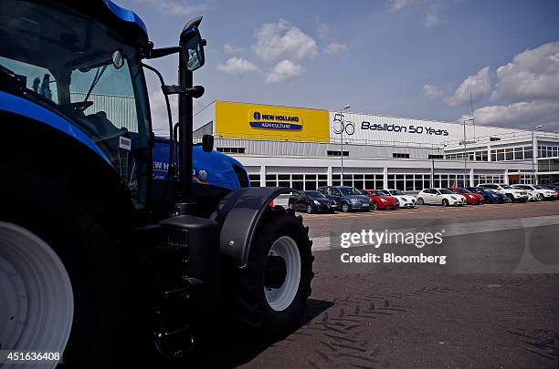 Newly manufactured New Holland tractor drives past a row of parked Alfa Romeo and Chrysler automobiles, outside the entrance to CNH Industrial NV's...