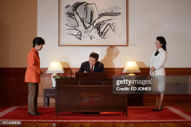 China's President Xi Jinping signs a guest book as his wife, Peng Liyuan watches, prior to attending a summit meeting with his South Korean...