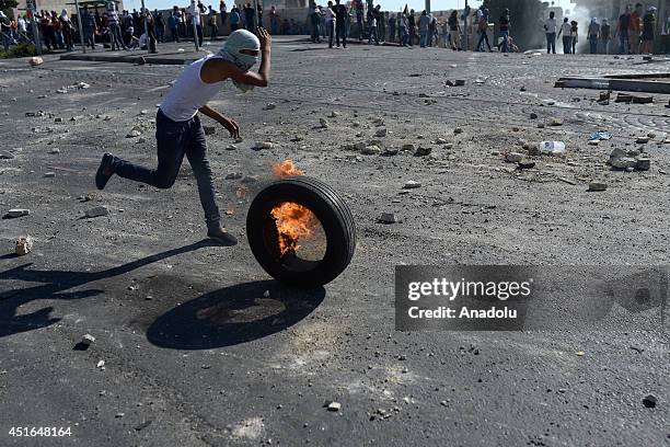 Palestinian youth rolls a burning tire towards Israeli security forces during the clashes over the abduction and killing of a Palestinian teen by...