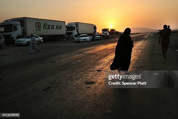 An Iraqi woman walks along a road where families who fled recent fighting near the city of Mosul are sleeping on the ground as they try to enter a...