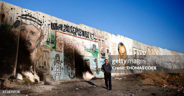 Palestinian man walks in front of a section of the Israeli separation barrier breaing a mural of late Palestinian leader Yasser Arafat and jailed...