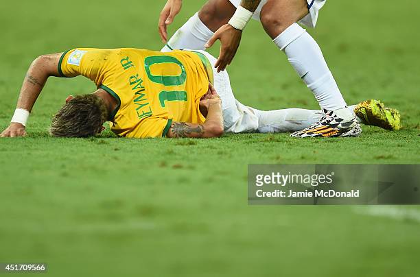 Neymar of Brazil lies on the field after a challenge as teammate Marcelo reacts during the 2014 FIFA World Cup Brazil Quarter Final match between...