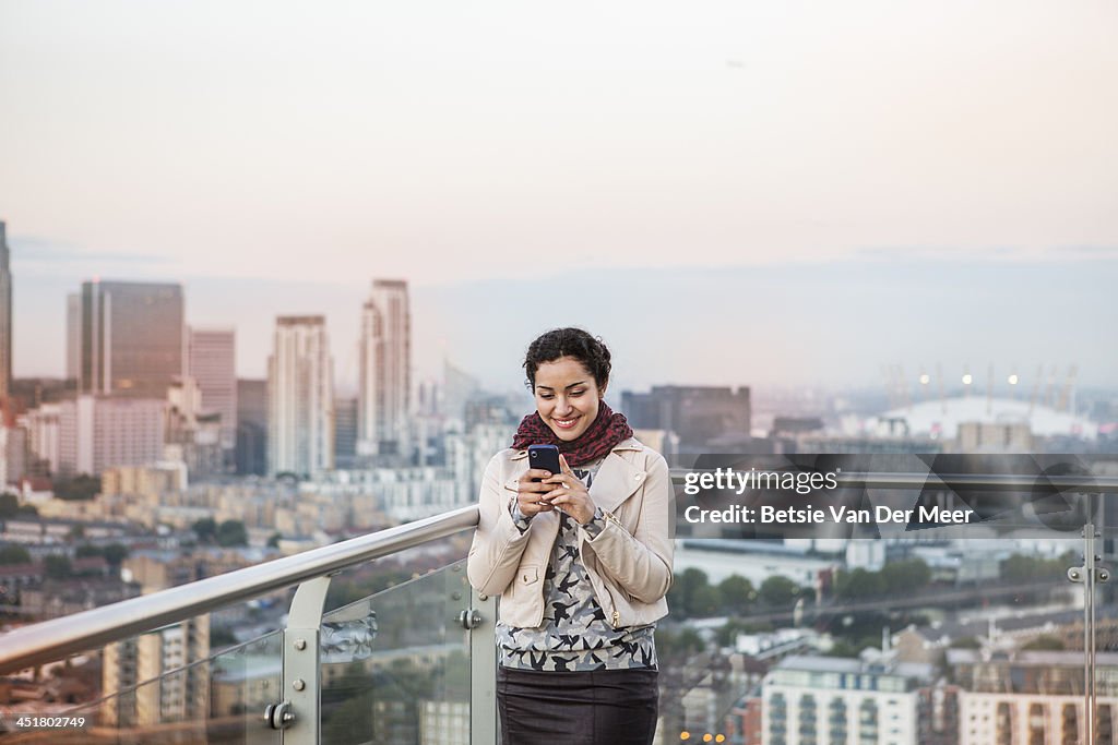 Woman looking at mobile phone, city in background.