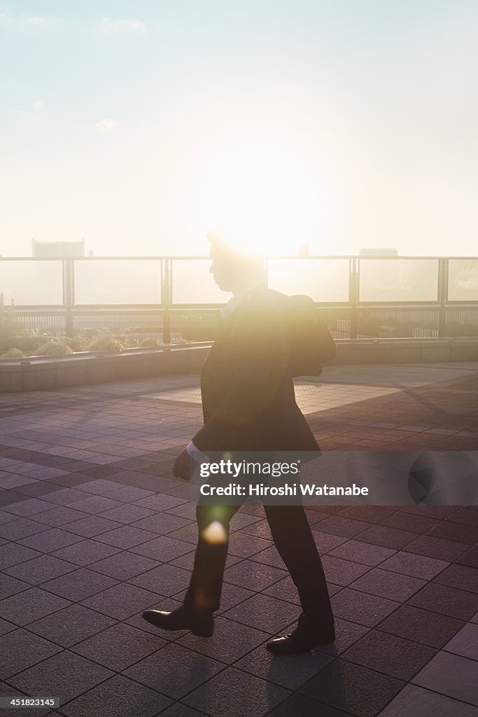 Businessman walking on the pavement at sunset