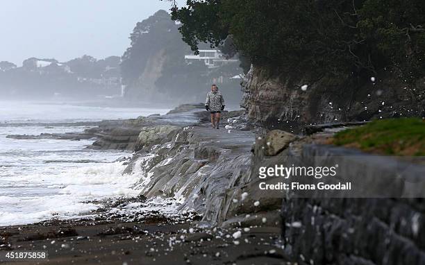 Man walks along the shoreline as sea foam blows up the beach from gale force winds on July 9, 2014 in Auckland, New Zealand. A severe weather warning...