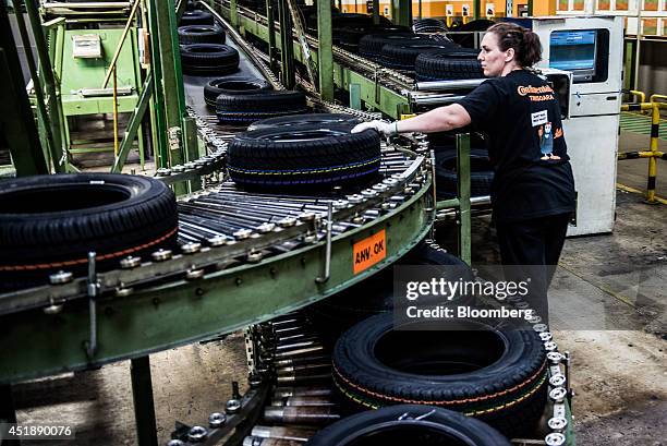 Worker inspects newly manufactured automobile tires as they move along conveyor belts at the Continental AG automobile tire manufacturing plant in...