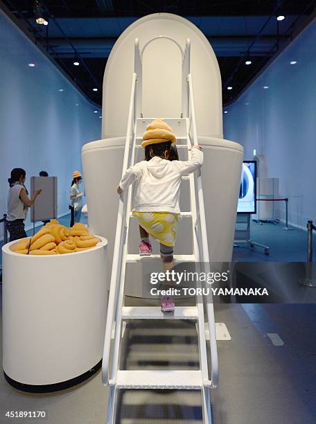 Child wearing a poo-shaped hat walks up stairs to climb on a giant toilet slide at a toilet exhibition at the National Museum of Emerging Science and...