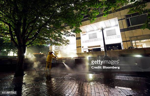 Worker uses water from a power washer to clean the cobbled floor of a seating area in the Canary Wharf business, finance and shopping district at...