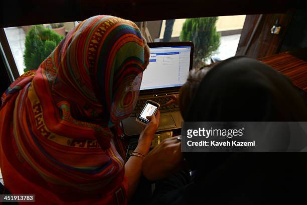 Two girls sit in a north Tehran coffee shop using Facebook and looking on the mobile phone at online fashion clothing in Tehran, Iran on October 13,...