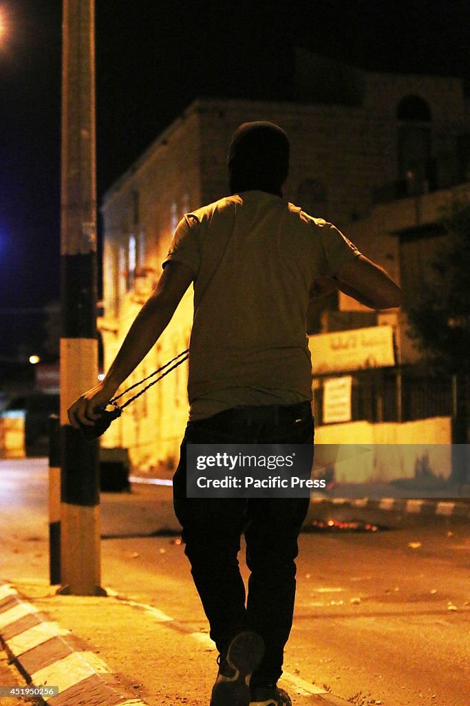 A masked Palestinian youth gets ready to launch a rock from...
