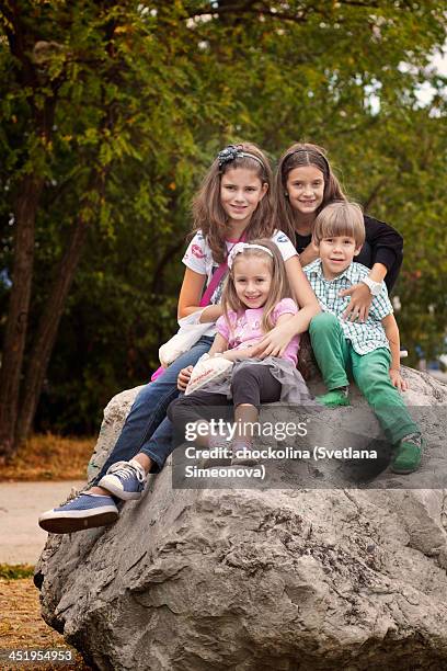 group photo of four children sitting on a rock - front view portrait of four children sitting on rock stock pictures, royalty-free photos & images