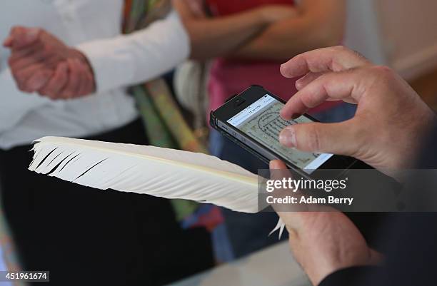 Rabbi and Torah Scribe Reuven Yaacobov looks at one of his hand-written illustrative works on an Apple iPhone as he holds his quill pen on July 10,...