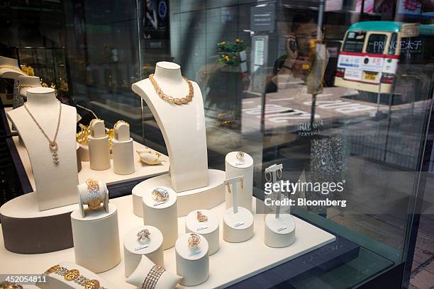 Woman on a mobile device looks at gold jewelry displayed in the window of a Chow Tai Fook Jewellery Group Ltd. Store in the shopping district of Tsim...