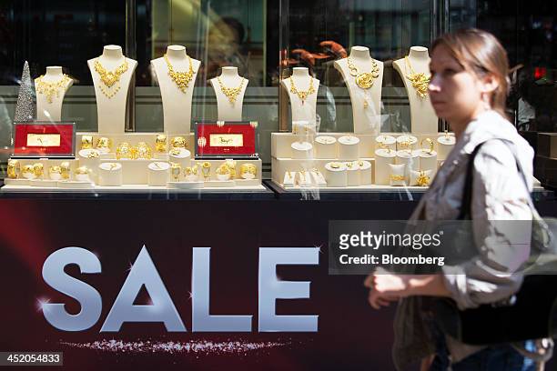 Woman walks past a sale sign displayed below gold jewelry in the window of a Chow Tai Fook Jewellery Group Ltd. Store in the shopping district of...