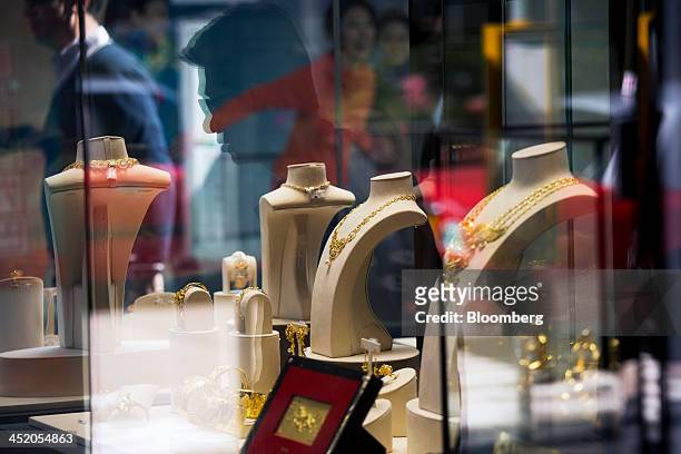 Gold jewelry sits on display as pedestrians are reflected in the window of a Chow Tai Fook Jewellery Group Ltd. Store in the shopping district of...
