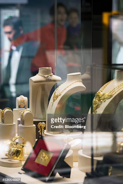 Gold jewelry sits on display as a pedestrian is reflected in the window of a Chow Tai Fook Jewellery Group Ltd. Store in the shopping district of...