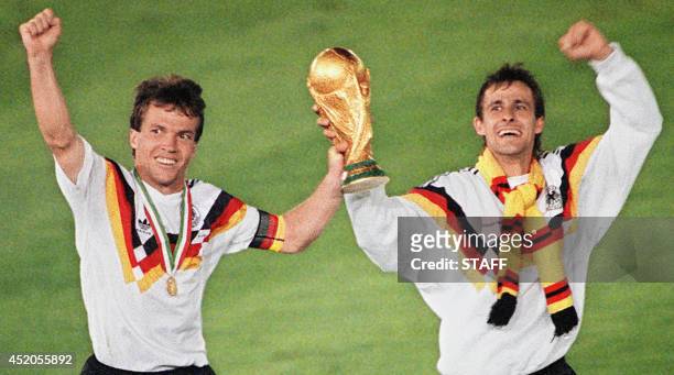 West German midfielder Lothar Matthaeus and forward Pierre Littbarski celebrate with the World Cup trophy after their team beat the defending...
