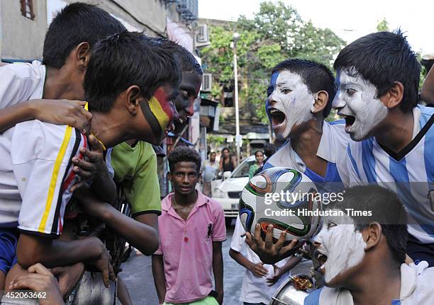 Indian boys with their faces painted and dressed in colours of German and Argentinean football teams pose for camera ahead of FIFA World Cup final...