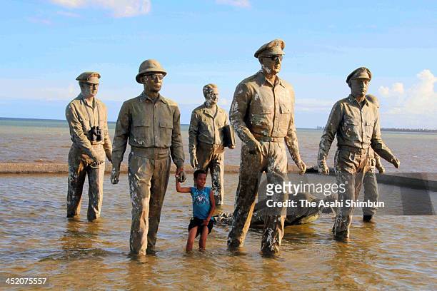 Boy plays at the McArthur Landing Memorial, which one of the statues of soldiers is toppled by the Typhoon Haiyan on November 25, 2013 in Palo,...