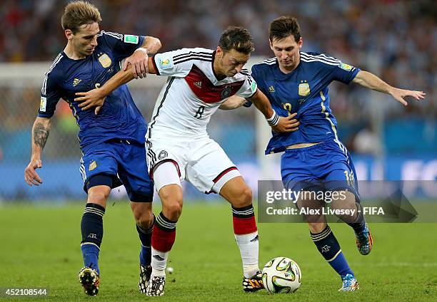 Mesut Oezil of Germany, Lucas Biglia and Lionel Messi of Argentina compete for the ball during the 2014 FIFA World Cup Brazil Final match between...