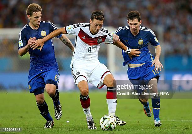 Mesut Oezil of Germany, Lucas Biglia and Lionel Messi of Argentina compete for the ball during the 2014 FIFA World Cup Brazil Final match between...