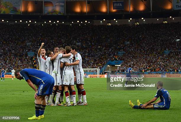 Mario Goetze of Germany celebrates scoring his team's first goal with teammates as a dejected Pablo Zabaleta and Javier Mascherano of Argentina look...