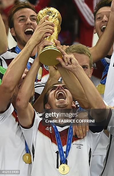 Germany's defender and captain Philipp Lahm holds up the World Cup trophy as he celebrates with his teammates after they won the 2014 FIFA World Cup...
