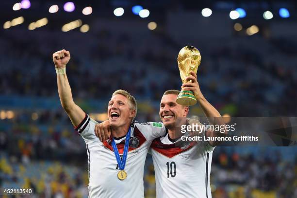 Bastian Schweinsteiger and Lukas Podolski of Germany celebrate with the World Cup trophy after defeating Argentina 1-0 in extra time during the 2014...