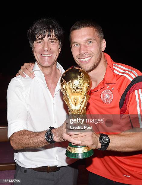 Germany head coach Joachim Loew and Lukas Podolski pose with the World Cup trophy as they celebrate with teammates at a party, after winning the 2014...