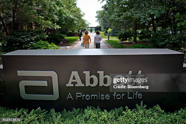 Employees walk near an Abbott Laboratories sign at the company's headquarters complex in Abbott Park, Illinois, U.S., on Monday, July 14, 2014....