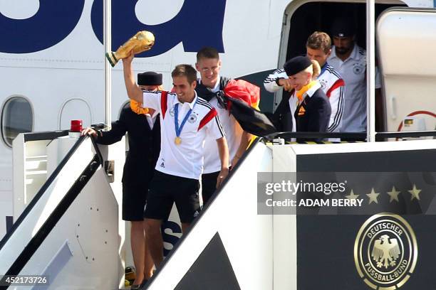 Germany's defender Philipp Lahm holds the World Cup as he and Germany's midfielder Bastian Schweinsteiger get off their airplane at Berlin airport...