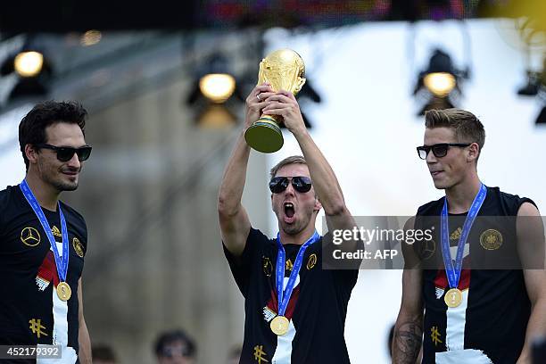 Germany's defenders Mats Hummels and Erik Durm watch Germany's captain Philipp Lahm celebrate with the trophy during a victory parade of Germany's...