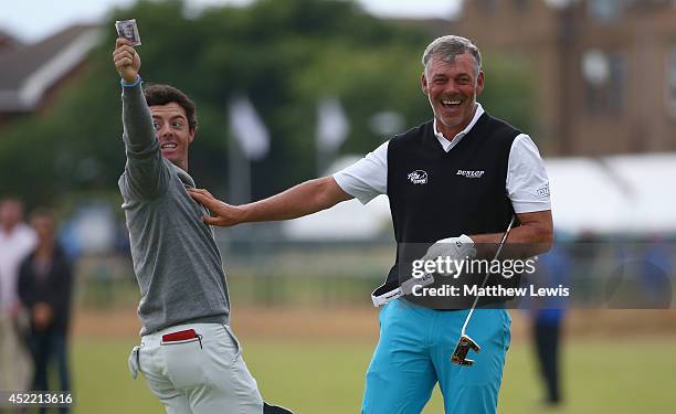 Rory McIlroy of Northern Ireland takes a bank note in celebration of winning a bet against Darren Clarke after their practice round prior to the...