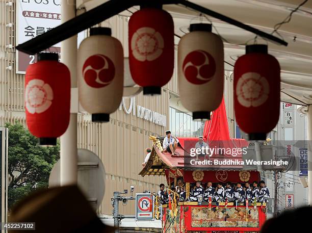 Japanese men dressed in traditional costumes sit on the roof top of festival cart named Yamahoko as others perform music during the annual Kyoto Gion...