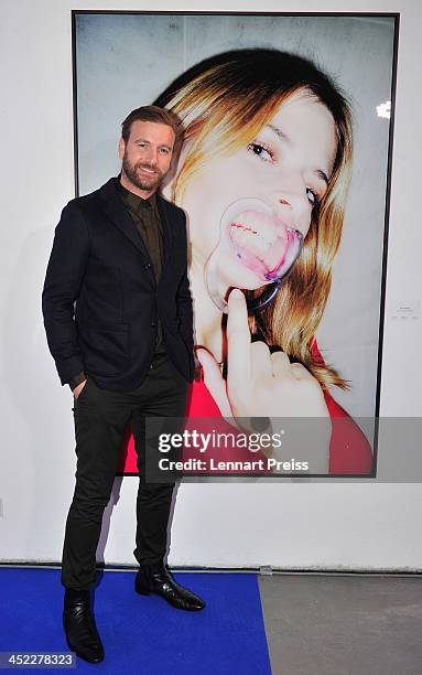 Artist Niels Ruf poses during his photography exhibition "Bitte recht freundlich" in front of a photograph of model Eva Padberg on November 27, 2013...