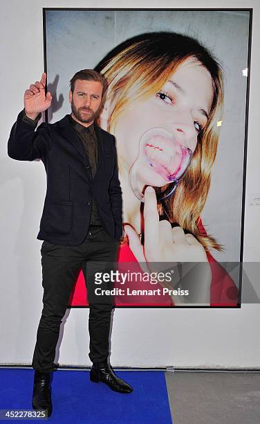 Artist Niels Ruf poses during his photography exhibition "Bitte recht freundlich" in front of a photograph of model Eva Padberg on November 27, 2013...