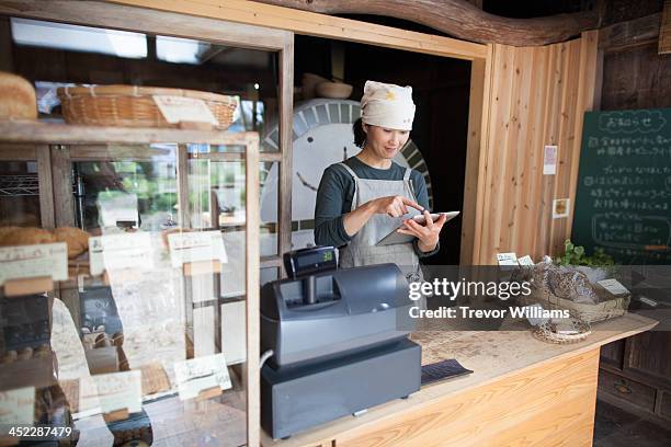 woman using tablet computer in asmall bakery - baker occupation stock pictures, royalty-free photos & images