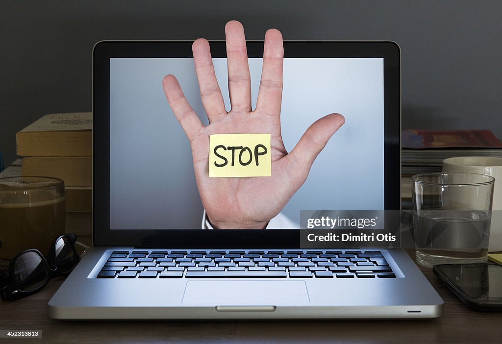 Stop hand appearing out of Laptop computer screen