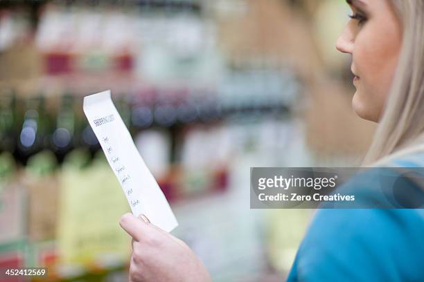 young woman looking at shopping list in supermarket - einkaufszettel stock-fotos und bilder