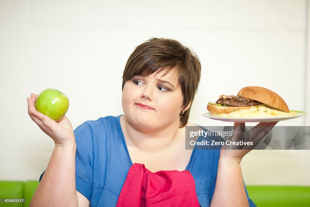 Young woman choosing between an apple and a burger